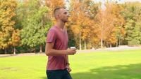 Young Man Walks in Park Holding a Cup of Coffee
