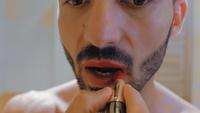 Guy se pinta los labios con lápiz labial rojo